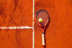 Tennis racket and ball on red clay court, ideal for sports-themed content.