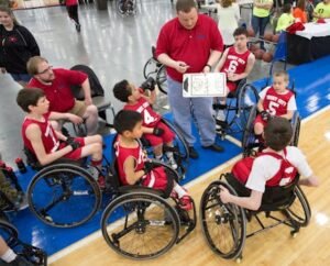 Young wheelchair basketball players and coach strategize during a game in Louisville.