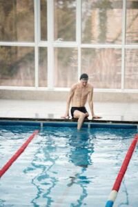A determined male swimmer with an amputee leg at an indoor poolside training session.