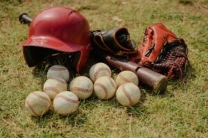 A collection of baseball gear including balls, a bat, helmet, and gloves on a grassy field.